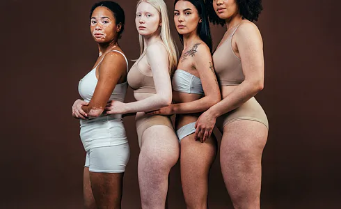 Čtyři ženy různých etnik, typů těla a pigmentace stojí vedle sebe v spodním prádle, symbolizující rozmanitost a přijetí tělesných rozdílů.